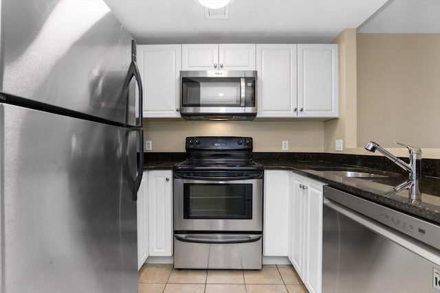 kitchen featuring sink, light tile patterned floors, appliances with stainless steel finishes, dark stone countertops, and white cabinets