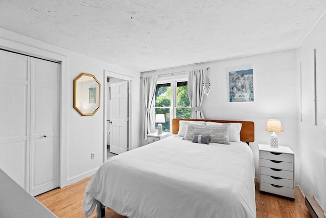 bedroom with light hardwood / wood-style flooring, a baseboard radiator, and a closet