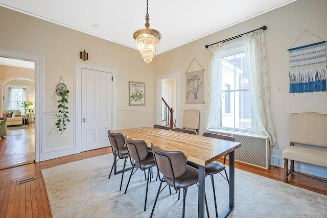 dining room featuring arched walkways, radiator, an inviting chandelier, and wood finished floors