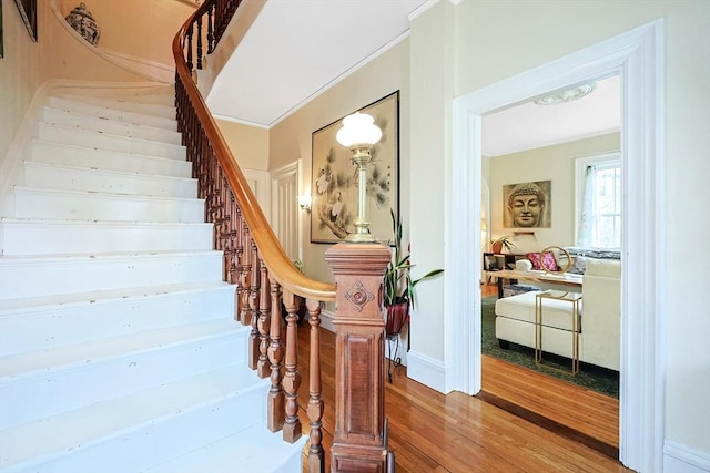 stairway with crown molding and wood finished floors