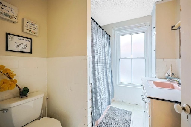 full bath featuring tile walls, a wainscoted wall, toilet, vanity, and a textured ceiling