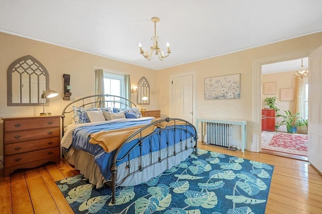 bedroom with hardwood / wood-style floors, a chandelier, radiator heating unit, and ornamental molding