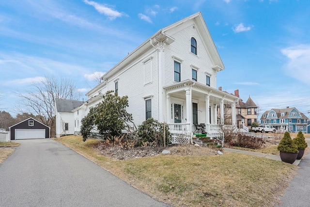 view of front of house with a residential view, a front yard, covered porch, a garage, and an outbuilding