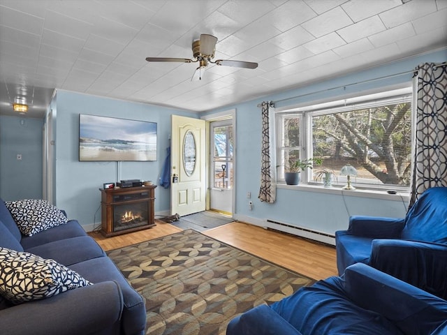 living room with a ceiling fan, wood finished floors, a lit fireplace, a baseboard radiator, and baseboards