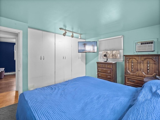 bedroom featuring rail lighting, wood finished floors, a closet, a wall mounted AC, and a baseboard radiator