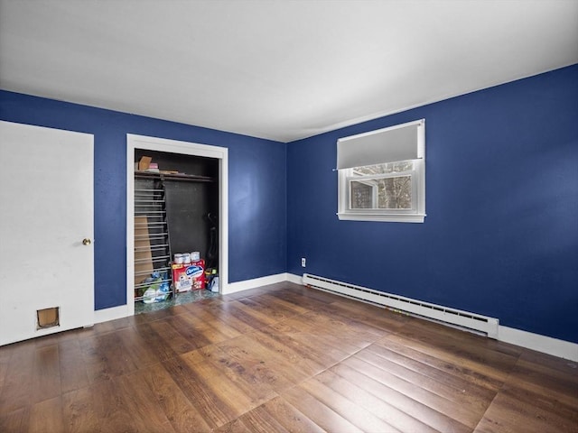 unfurnished bedroom with a baseboard heating unit, baseboards, a closet, and wood finished floors