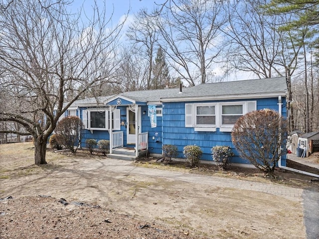 view of front of home with dirt driveway and a shingled roof