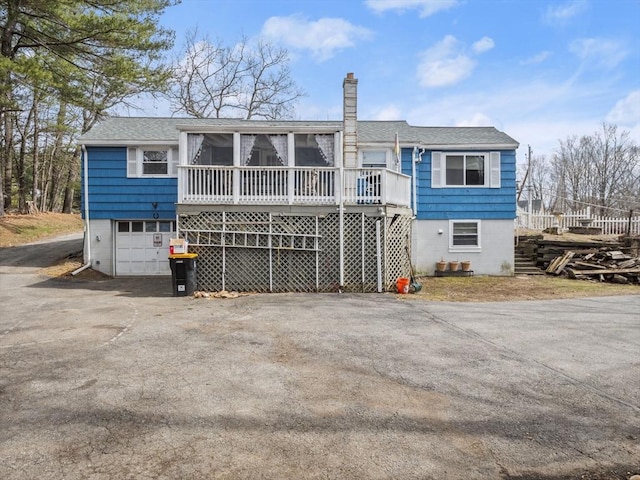 back of property with aphalt driveway, an attached garage, a chimney, and a sunroom