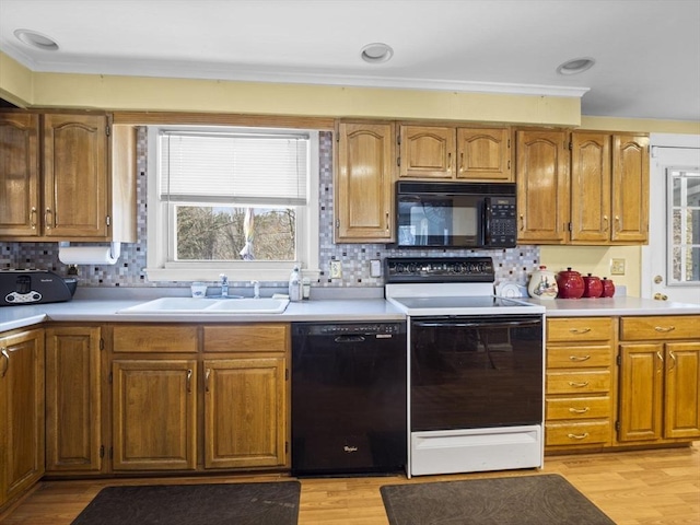 kitchen with light wood finished floors, black appliances, light countertops, and a sink