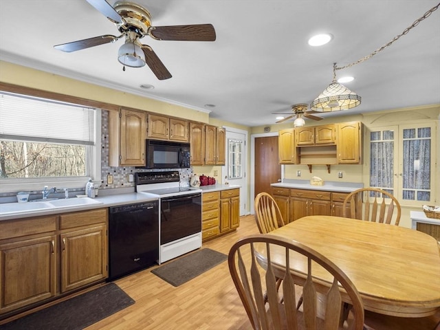 kitchen featuring backsplash, light countertops, light wood-style floors, black appliances, and a sink