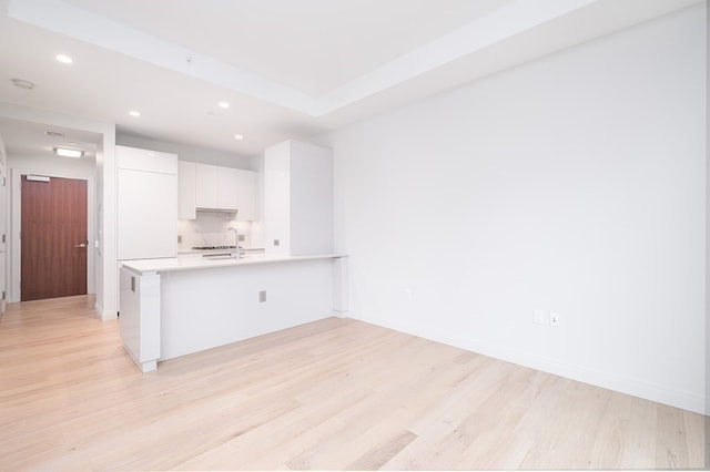 kitchen with white cabinets, backsplash, kitchen peninsula, light hardwood / wood-style flooring, and sink