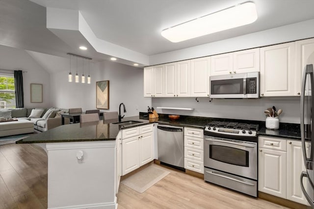 kitchen featuring stainless steel appliances, a sink, a peninsula, light wood finished floors, and white cabinets