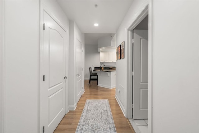 hall featuring light wood finished floors, recessed lighting, and baseboards