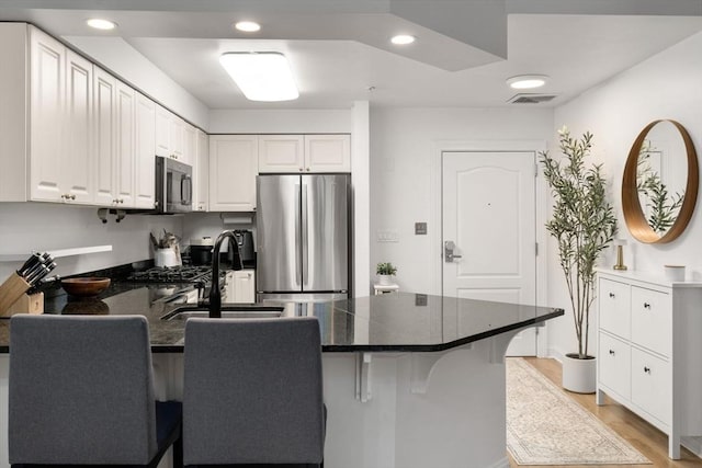 kitchen featuring stainless steel appliances, a peninsula, dark countertops, a kitchen bar, and recessed lighting