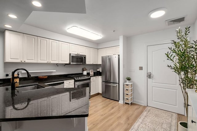 kitchen featuring stainless steel appliances, a sink, dark stone counters, light wood-style floors, and white cabinets