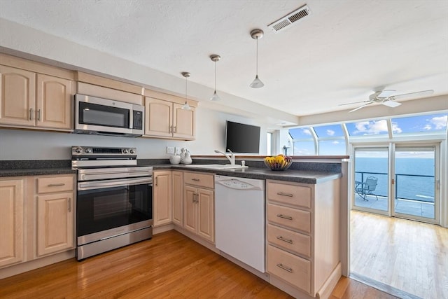 40 Oceanside Dr Unit 40, Hull, MA 02045 - kitchen featuring stainless steel appliances, a peninsula, light wood-type flooring, dark countertops, and light brown cabinetry