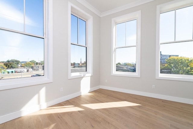 empty room with baseboards, crown molding, and wood finished floors