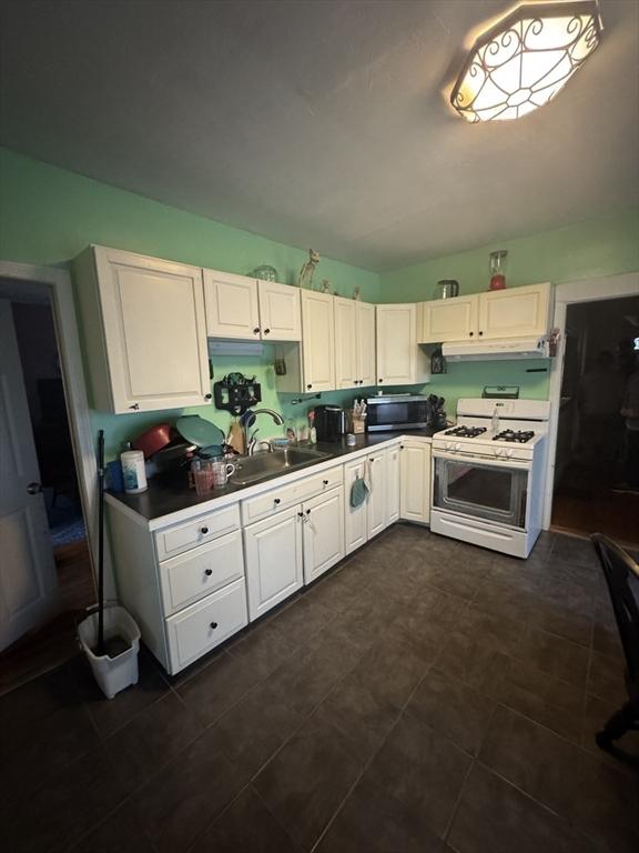 kitchen featuring white gas range oven, stainless steel microwave, under cabinet range hood, a sink, and white cabinetry
