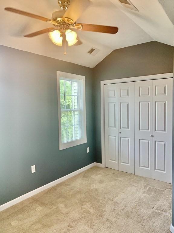 unfurnished bedroom with light carpet, vaulted ceiling, a closet, a ceiling fan, and baseboards