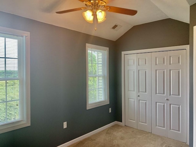unfurnished bedroom with light carpet, lofted ceiling, a closet, baseboards, and a ceiling fan