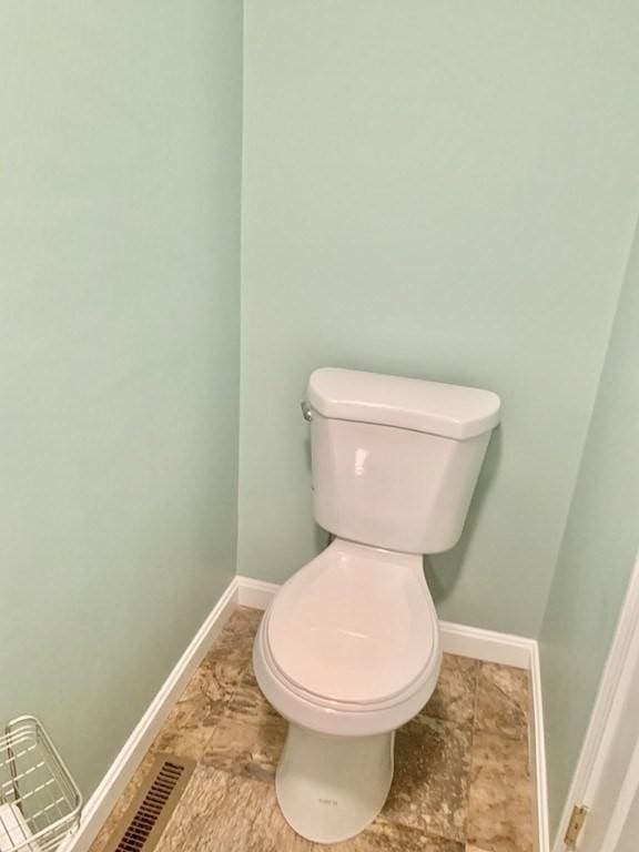 bathroom featuring baseboards, stone finish floors, and toilet