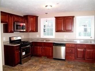 kitchen featuring appliances with stainless steel finishes, light countertops, a sink, and reddish brown cabinets