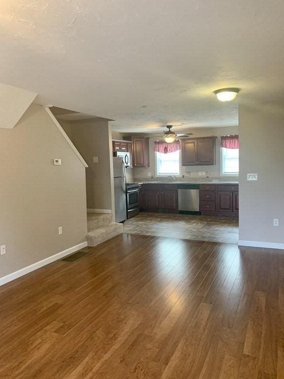 unfurnished living room featuring baseboards, dark wood-type flooring, and a ceiling fan