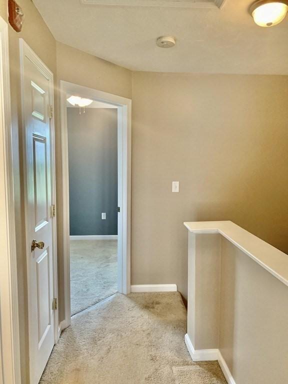 hallway featuring an upstairs landing, carpet floors, and baseboards