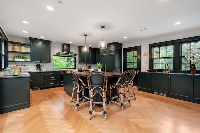 kitchen with a center island, open shelves, dark countertops, backsplash, and wall chimney exhaust hood