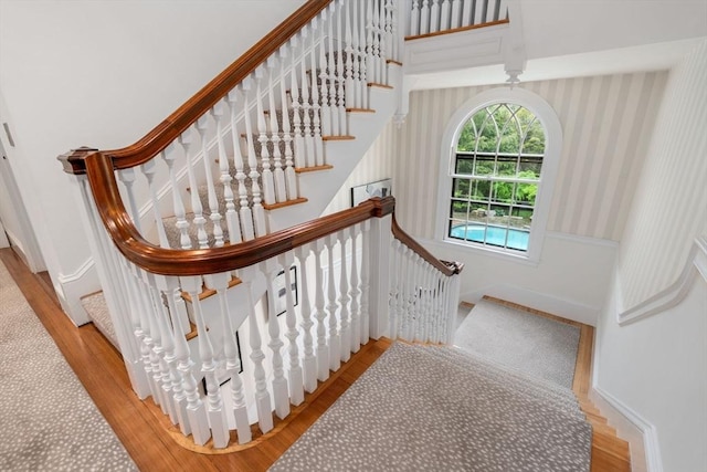 staircase featuring wallpapered walls, baseboards, and wood finished floors