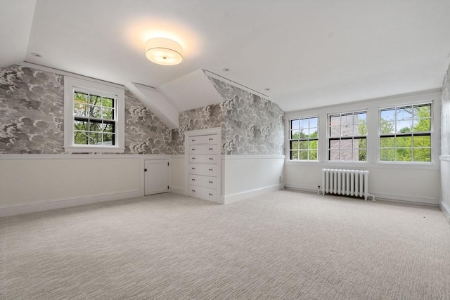 additional living space with light colored carpet, a wainscoted wall, baseboards, vaulted ceiling, and radiator heating unit