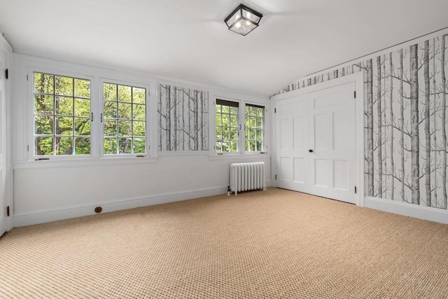 empty room featuring lofted ceiling, radiator heating unit, carpet flooring, and baseboards