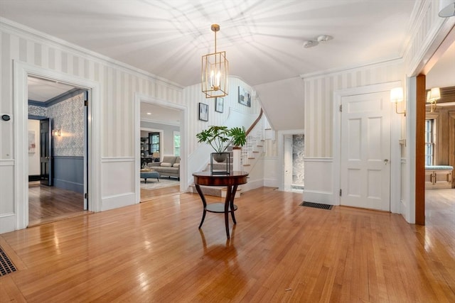 entryway featuring a wainscoted wall, ornamental molding, light wood-style flooring, and wallpapered walls