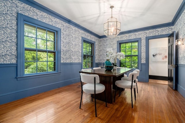 dining room with ornamental molding, wood-type flooring, a wainscoted wall, and wallpapered walls