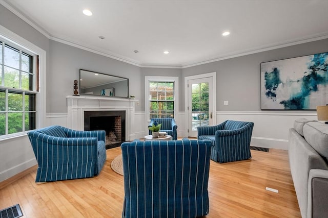 living area featuring visible vents, light wood-style floors, ornamental molding, a fireplace with flush hearth, and wainscoting