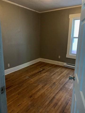 empty room with baseboard heating, crown molding, and dark hardwood / wood-style flooring