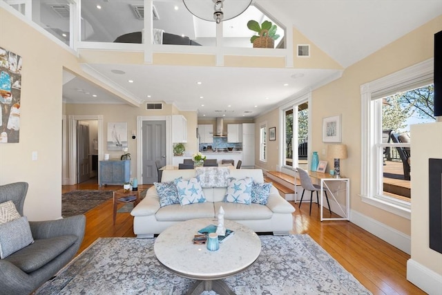 living room featuring a towering ceiling, light wood-style floors, ornamental molding, recessed lighting, and baseboards