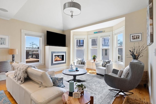 living area with light wood-style flooring, a glass covered fireplace, and high vaulted ceiling