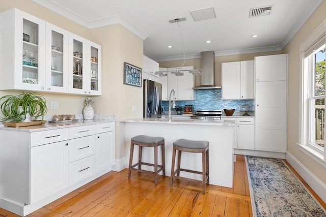 kitchen featuring wall chimney exhaust hood, stainless steel fridge with ice dispenser, light wood finished floors, white cabinetry, and ornamental molding