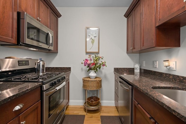 kitchen featuring appliances with stainless steel finishes, light wood-type flooring, baseboards, dark stone countertops, and a sink
