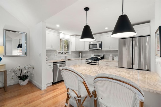 kitchen with a sink, white cabinetry, appliances with stainless steel finishes, light wood finished floors, and decorative backsplash