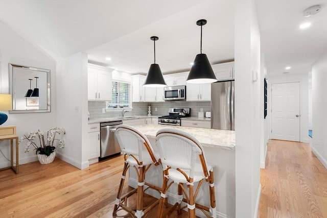 kitchen with light wood finished floors, light stone countertops, stainless steel appliances, white cabinetry, and a sink