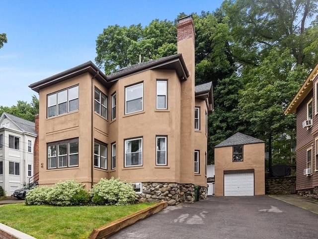 view of side of property featuring a garage, driveway, a chimney, an outbuilding, and stucco siding