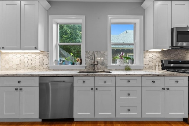 kitchen with appliances with stainless steel finishes, a sink, white cabinets, and backsplash