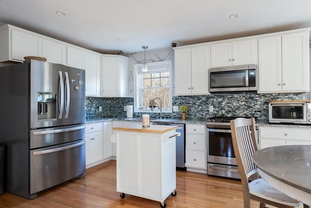 kitchen with light wood-style flooring, stainless steel appliances, a kitchen island, white cabinetry, and decorative backsplash