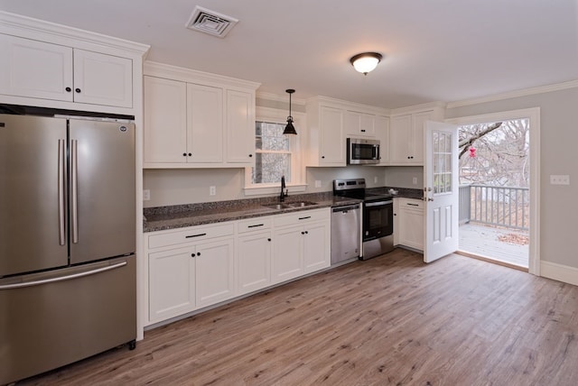 kitchen featuring appliances with stainless steel finishes, sink, light hardwood / wood-style floors, white cabinetry, and hanging light fixtures