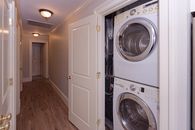 clothes washing area with stacked washer and dryer, wood-type flooring, and ornamental molding