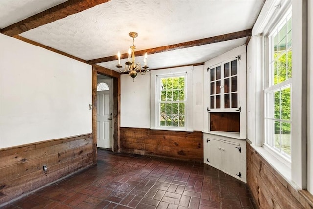 empty room featuring wood walls, a chandelier, brick flooring, healthy amount of natural light, and a wainscoted wall