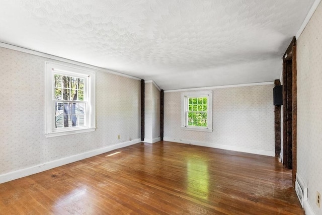 unfurnished room featuring wood finished floors, a textured ceiling, wallpapered walls, crown molding, and baseboards