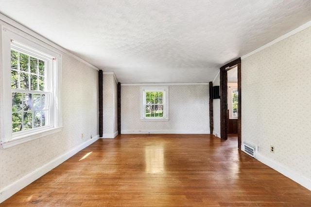 empty room with ornamental molding, wallpapered walls, light wood-style flooring, baseboards, and a textured ceiling